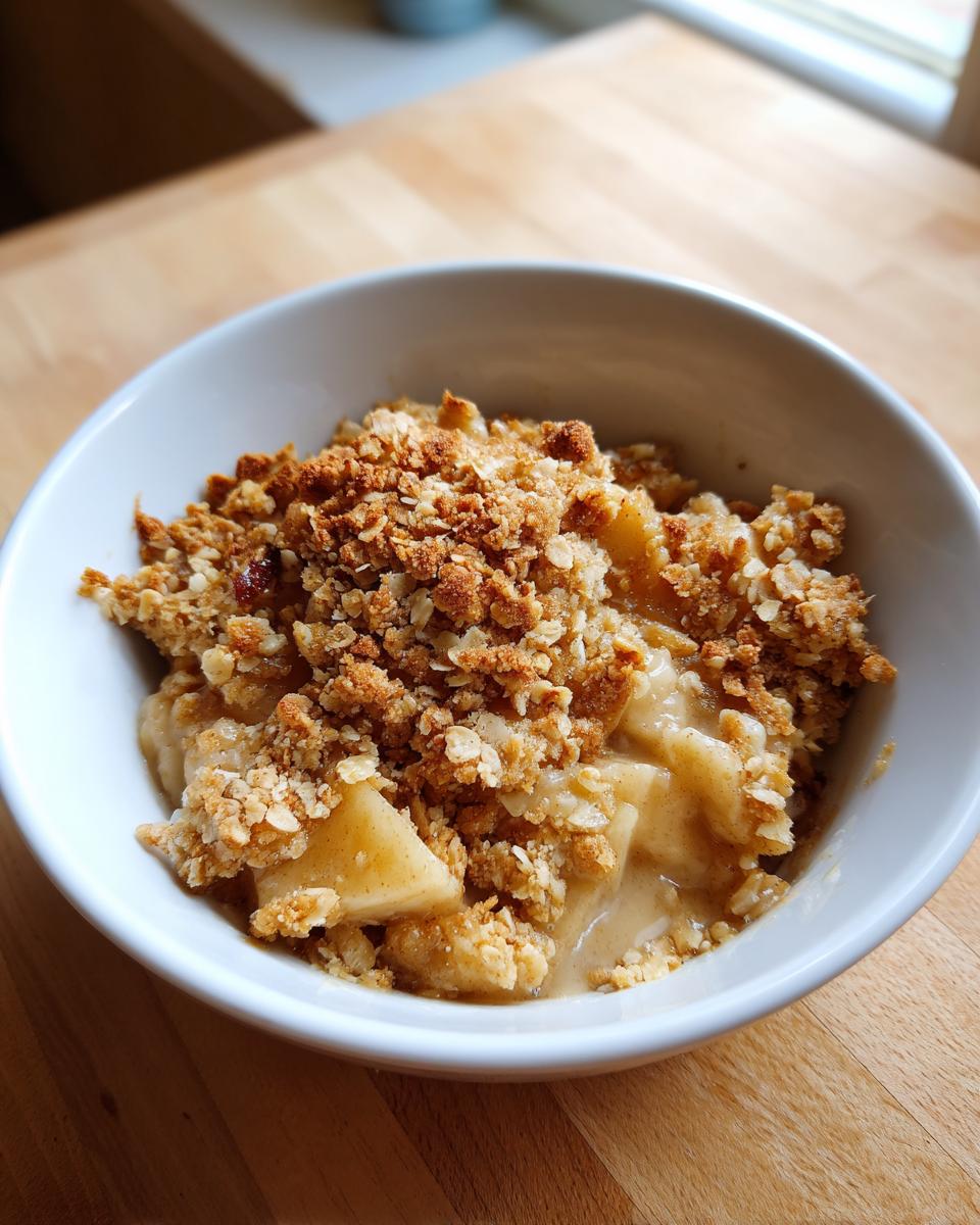 Close-up of a warm serving of amazing apple crumble with a thick oat topping in a white bowl.