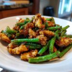 Close-up of crispy chicken pieces coated in sauce mixed with vibrant green beans in a chicken and green bean stir fry.