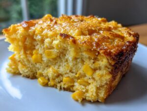 Close-up of a moist, golden slice of corn casserole recipe, studded with whole corn kernels.