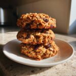 A stack of three golden brown oatmeal raisin cookies resting on a small white plate.