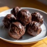 A close-up of several rich, chocolate-covered oreo balls stacked on a white plate.