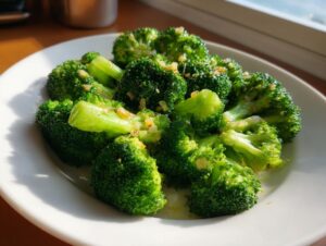 Bright green, perfectly cooked steamed broccoli florets seasoned with minced garlic on a white plate.