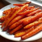 A close-up of perfectly glazed Balsamic Roasted Carrots piled high on a white plate.
