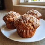 Three freshly baked banana nut muffins topped with coarse sugar, resting on a white plate.