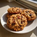 Close-up of four thick, chewy cowboy cookies loaded with oats, chocolate chips, and pecans on a white plate.