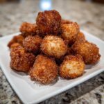 A close-up photo of a white plate piled high with freshly made churro donut bites coated in cinnamon sugar.