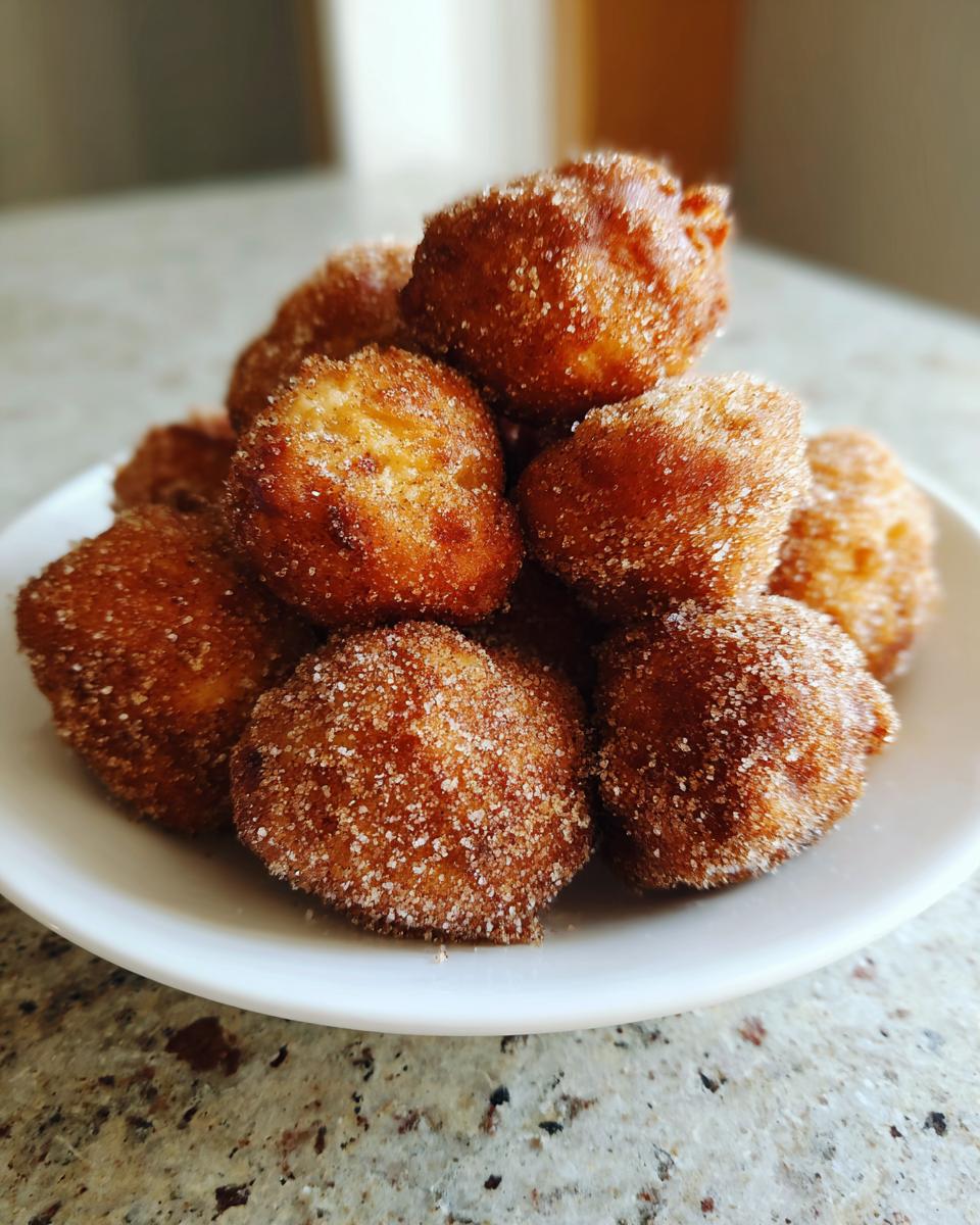 A close-up stack of freshly fried churro donut bites generously coated in cinnamon sugar.