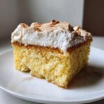 A moist slice of churro three milks cake topped with whipped cream and sprinkled with cinnamon.