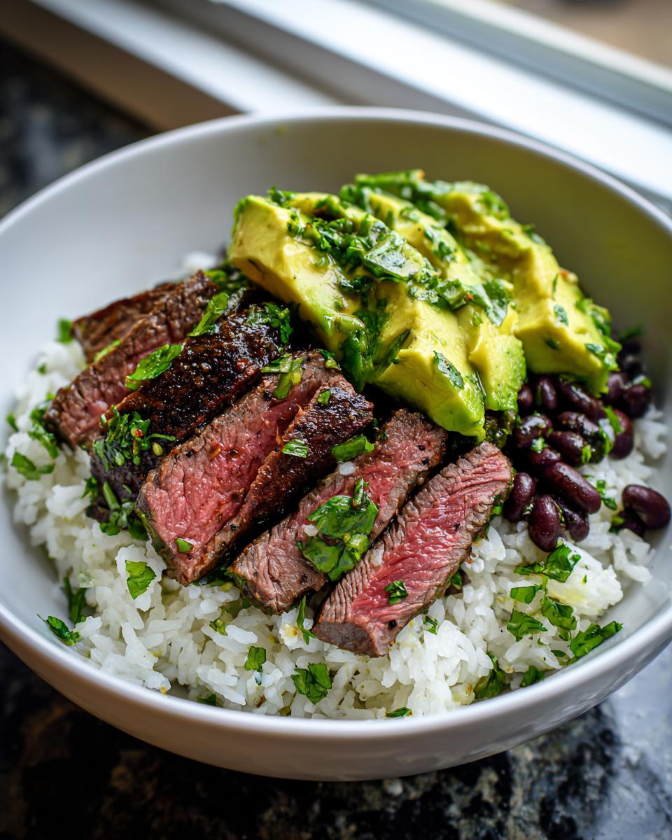 Close-up of medium-rare steak slices over rice in a bowl, topped with avocado and black beans for cilantro lime steak bowls.