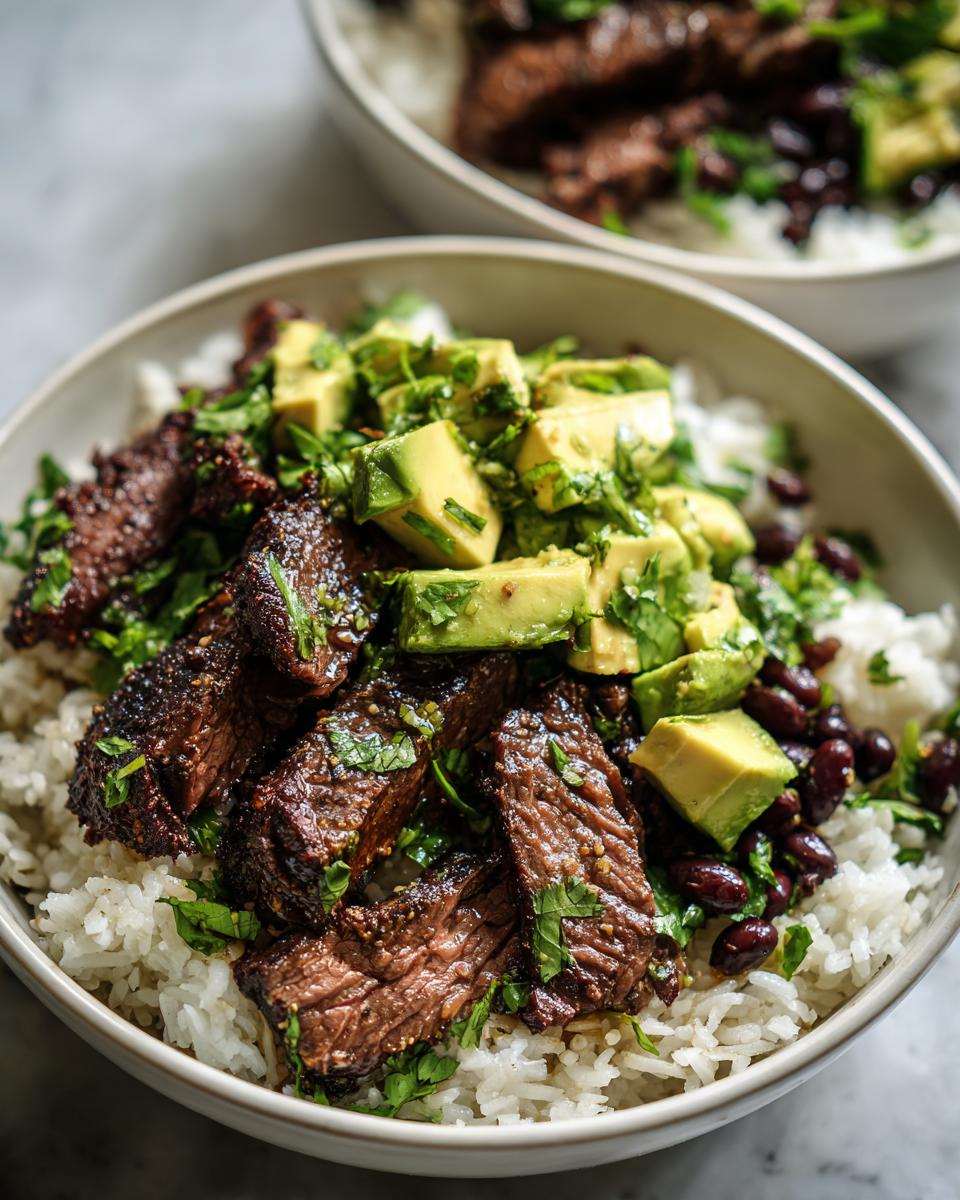 Close-up of a bowl filled with white rice, topped with sliced cilantro lime steak, black beans, and diced avocado.