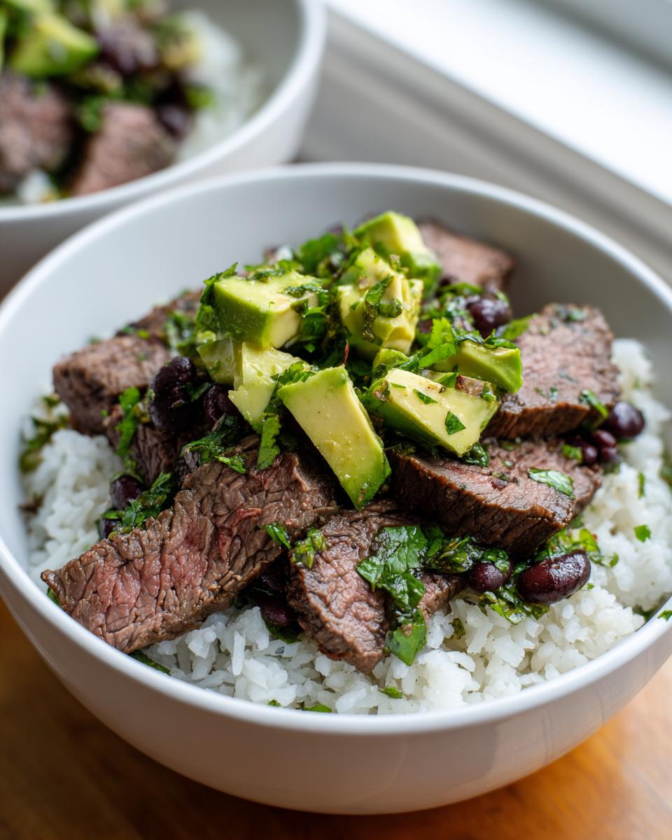 Close-up of sliced steak served over white rice, topped with black beans, avocado chunks, and cilantro lime dressing in a white bowl, ideal for cilantro lime steak bowls.