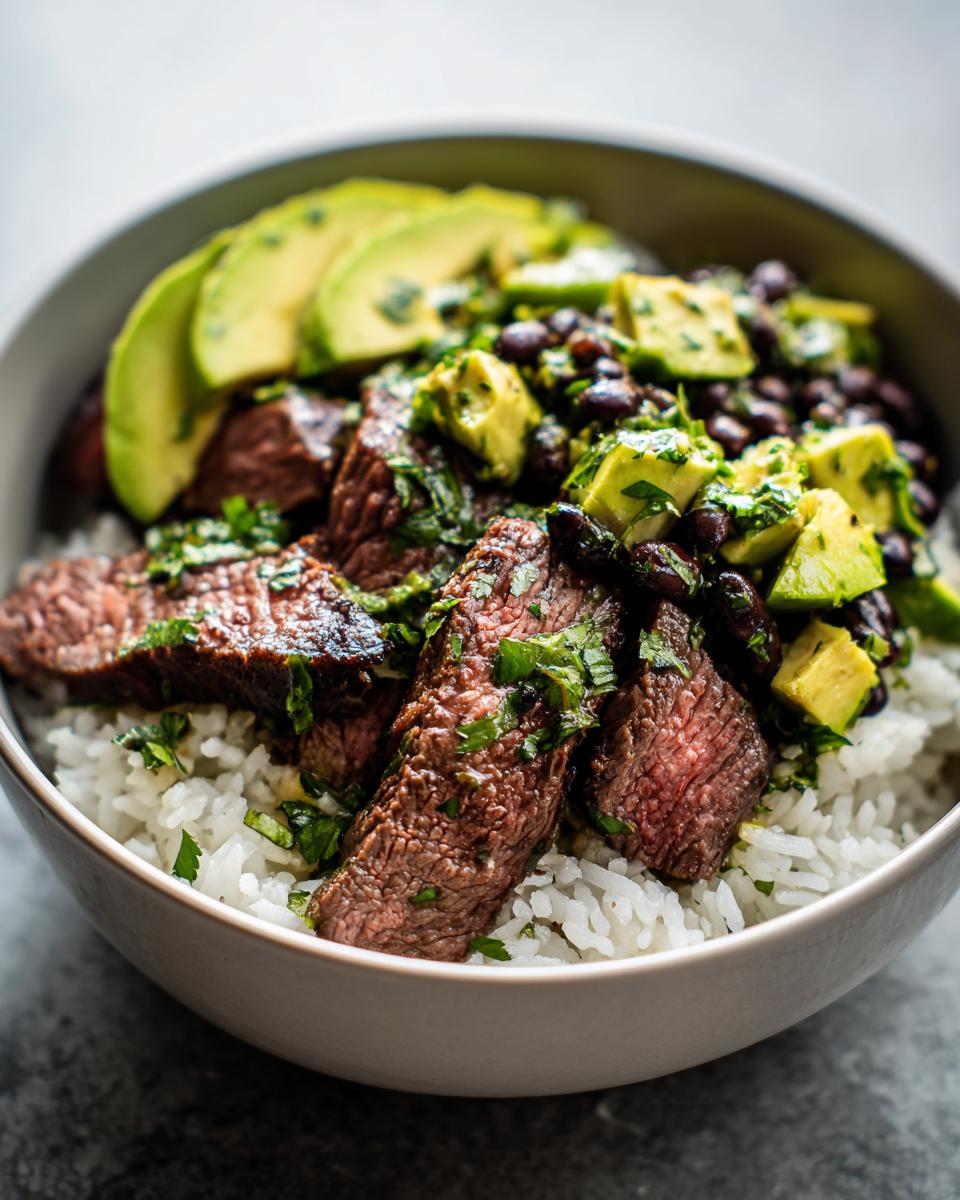 Close-up of perfectly cooked steak slices over white rice, topped with black beans, avocado, and cilantro lime dressing in cilantro lime steak bowls.