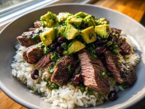 Close-up of sliced steak over white rice, topped with avocado chunks and black beans in a cilantro lime steak bowls recipe.
