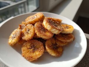 Close-up of freshly made cinnamon sugar air fryer banana chips piled on a white plate, glistening with sugar.