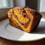 A thick slice of Cinnamon Swirl Pumpkin Bread showing vibrant orange pumpkin batter swirled with dark cinnamon filling, served on a white plate.