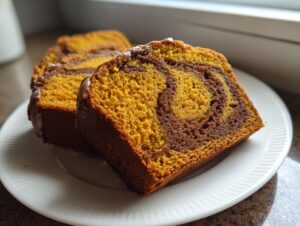 Two slices of moist Cinnamon Swirl Pumpkin Bread showing a beautiful orange and dark brown swirl pattern on a white plate.