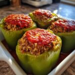 Four bright green Classic Stuffed Peppers filled with meat and rice, topped with tomato sauce.