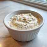 Close-up of creamy, chunky homemade blue cheese dip served in a small white fluted ramekin.