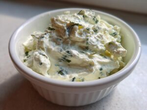 Close-up of a thick, creamy homemade blue cheese dip speckled with green herbs in a small white bowl.