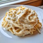 A close-up of creamy pasta coated in rich cottage cheese alfredo sauce, served on a white plate.
