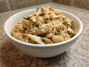 A close-up of creamy crockpot white chicken chili featuring shredded chicken and white beans, garnished with parsley.