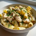 A close-up of a bowl filled with creamy garlic butter chicken rigatoni, topped with fresh parsley.
