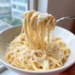 A fork lifts creamy spaghetti coated in sauce, showing a cheesy pull of amazing 20-Min parmesan pasta topped with grated cheese.