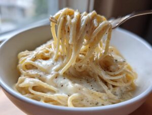 Close-up of spaghetti coated in creamy sauce being lifted from a bowl, highlighting the rich parmesan pasta texture.