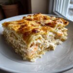 A close-up of a rich, creamy slice of seafood lasagna showing layers of pasta, white sauce, crab, and shrimp.