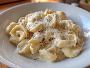 A close-up of a bowl filled with creamy Tortellini Alfredo Recipe, topped with grated Parmesan cheese and black pepper.