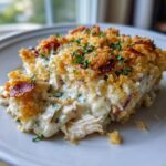 A close-up serving of creamy Dolly Parton Casserole featuring shredded chicken, a rich sauce, and a crunchy, golden-brown topping with bacon pieces.