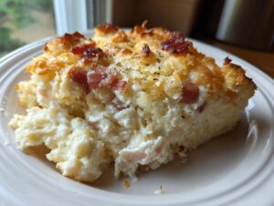 A close-up serving of the creamy Dolly Parton casserole featuring a golden-brown crust, visible bacon pieces, and a rich, cheesy interior.