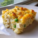 A close-up of a square slice of forgotten chicken and rice casserole with a golden, cheesy crust and visible peas.
