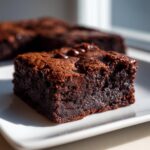 Close-up of a fudgy, dark chocolate square of amazing zucchini brownies on a white plate.