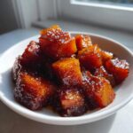 Close-up of perfectly glazed, cubed braised butternut pieces piled high in a small white bowl.