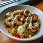 A white bowl filled with quinoa, corn, red peppers, topped with perfectly grilled shrimp bowls drizzled with green sauce.