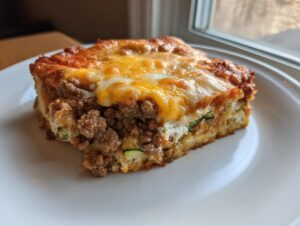 A close-up of a hearty slice of Ground Beef and Zucchini Casserole topped with melted golden cheese.