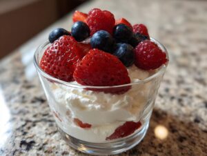 A glass serving of white, creamy high protein cheesecake fluff topped with fresh strawberries, blueberries, and raspberries.