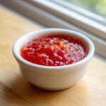 Close-up of vibrant red, chunky homemade cocktail sauce recipe served in a small white ramekin.