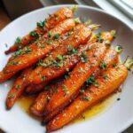 Close-up of glossy Honey Garlic Butter Roasted Carrots topped with minced garlic and parsley in a white serving dish.