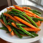A close-up of vibrant Honey Glazed Carrots and Green Beans tossed in a shiny glaze on a white plate.