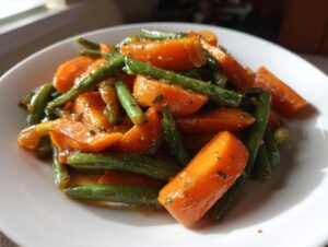 A close-up of bright orange carrots and vibrant green beans coated in a shiny glaze, served in a white bowl.