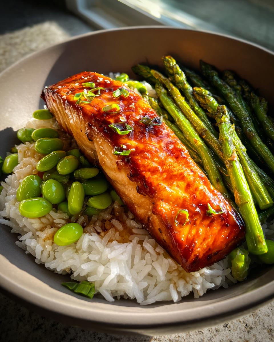 Close-up of a perfectly cooked honey glazed salmon bowl featuring rice, edamame, and roasted asparagus.