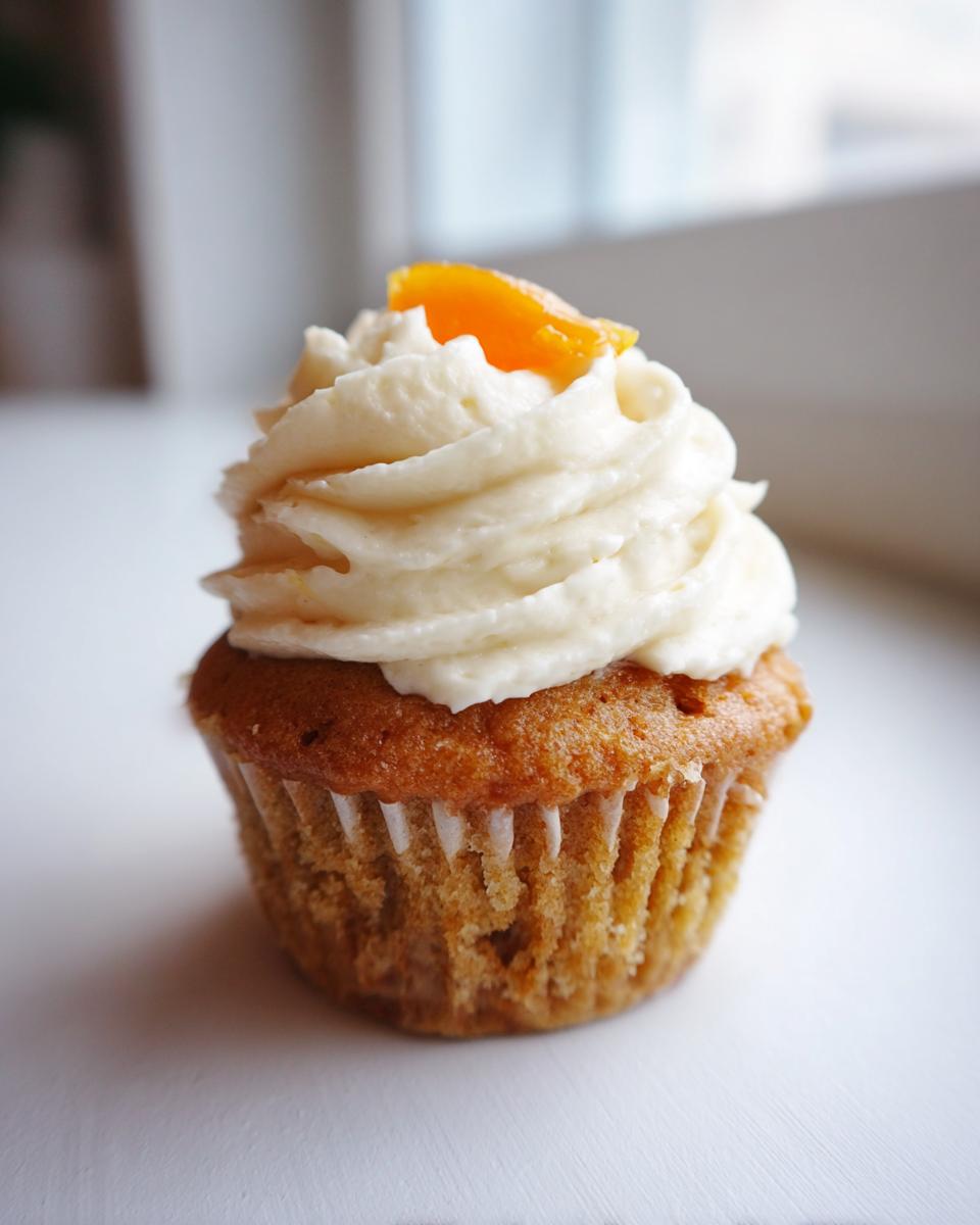 A single, beautifully frosted honey peach cream cheese cupcake topped with a small slice of dried peach.