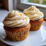 Close-up of two delicious honey peach cupcakes with swirls of light cream cheese frosting on a white plate.