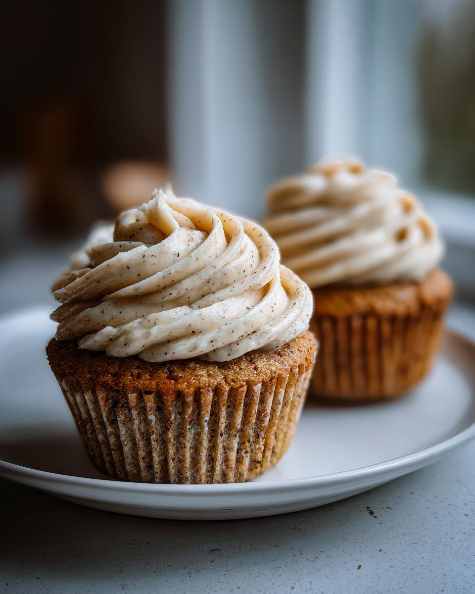 Two honey peach cupcakes with swirls of speckled cream cheese frosting sitting on a white plate.