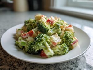 A close-up serving of creamy honeycrisp apple broccoli salad featuring bright green florets and diced red apples.