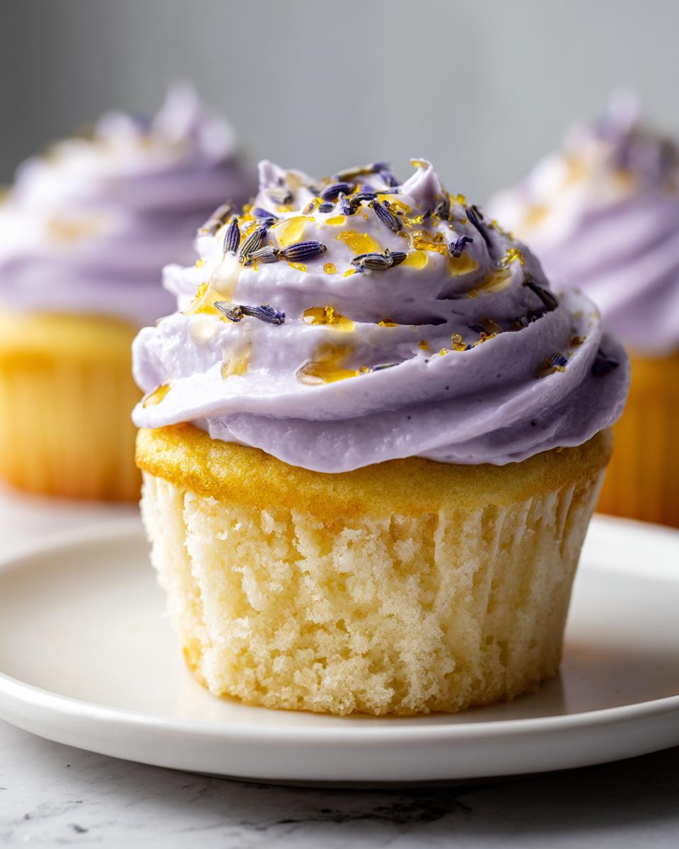 Close-up of a single lavender honey cupcake topped with light purple frosting, drizzled with honey, and sprinkled with dried lavender buds.