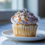 A single lavender honey cupcake with pale purple frosting, drizzled with honey and topped with dried lavender buds.