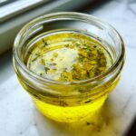 Close-up of bright yellow lemon dill vinaigrette mixed with fresh dill herbs in a small glass jar.